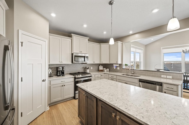 kitchen featuring stainless steel appliances, a sink, backsplash, light wood-style flooring, and lofted ceiling