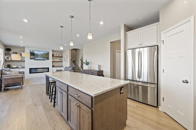 kitchen featuring freestanding refrigerator, open floor plan, light stone counters, a kitchen island, and recessed lighting