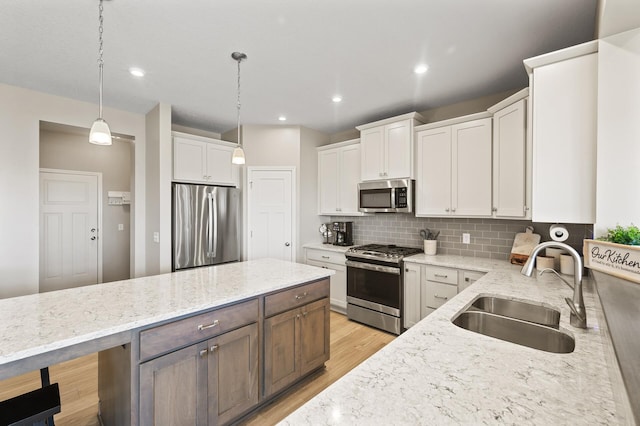 kitchen featuring appliances with stainless steel finishes, a sink, light wood-type flooring, decorative backsplash, and white cabinets