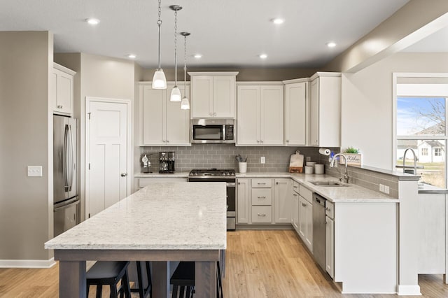 kitchen with stainless steel appliances, a sink, light wood-style flooring, decorative backsplash, and a center island