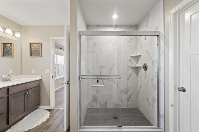 bathroom featuring a marble finish shower, vanity, wood finished floors, and baseboards