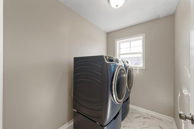 clothes washing area with separate washer and dryer, light marble finish floors, and baseboards