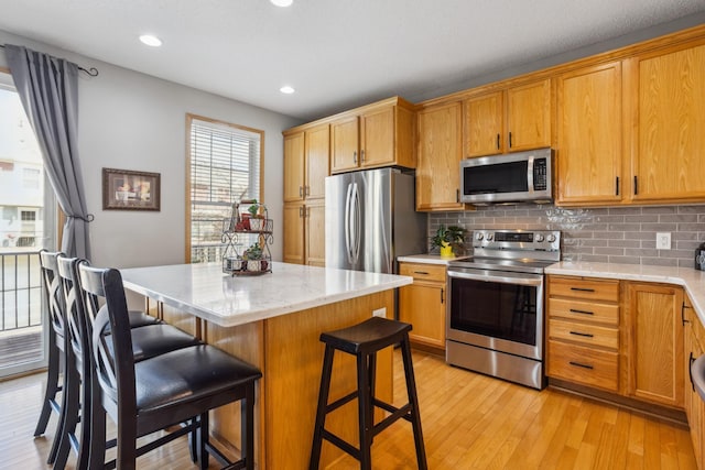kitchen with a kitchen breakfast bar, appliances with stainless steel finishes, tasteful backsplash, a center island, and light wood-style floors