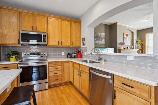 kitchen with a textured ceiling, tasteful backsplash, a sink, light wood finished floors, and stainless steel appliances