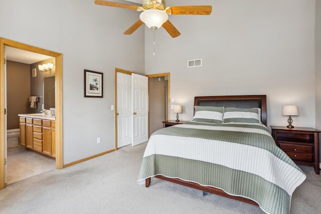 bedroom featuring a high ceiling, light carpet, baseboards, ensuite bathroom, and visible vents