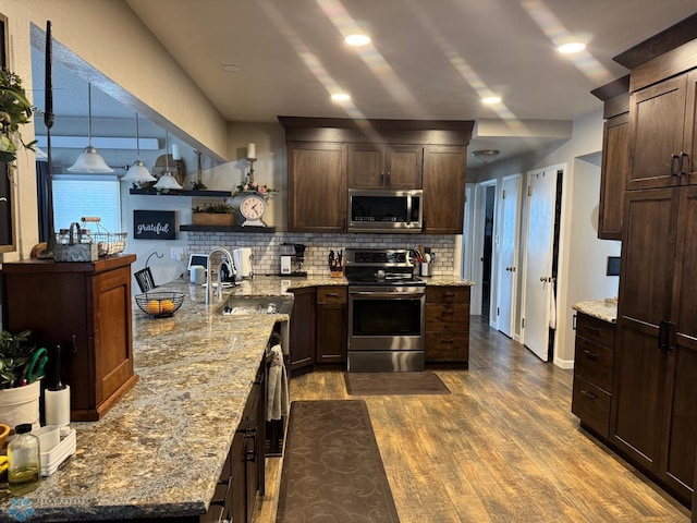 kitchen featuring appliances with stainless steel finishes, a sink, dark brown cabinets, dark wood finished floors, and decorative backsplash