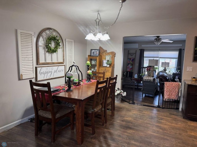 dining area featuring ceiling fan with notable chandelier, baseboards, and dark wood finished floors