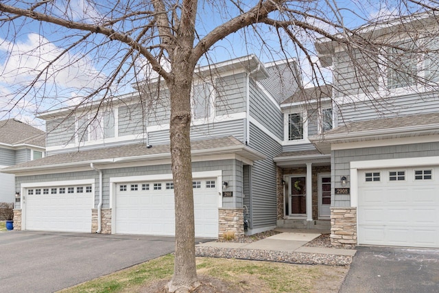 view of front of home featuring an attached garage, roof with shingles, aphalt driveway, and stone siding
