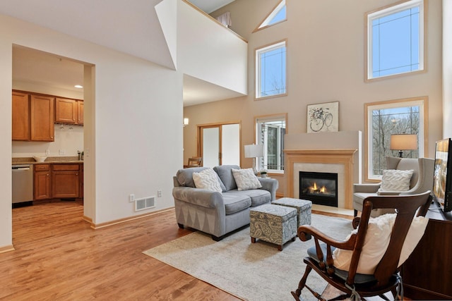 living area with a glass covered fireplace, visible vents, a high ceiling, light wood finished floors, and baseboards