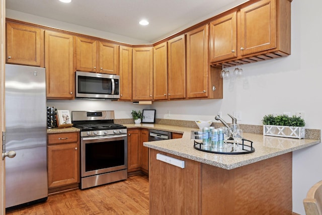 kitchen with a sink, light wood-type flooring, a peninsula, recessed lighting, and stainless steel appliances