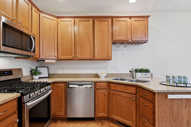 kitchen featuring brown cabinetry, light wood finished floors, a sink, and appliances with stainless steel finishes