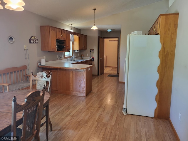 kitchen featuring freestanding refrigerator, light wood-style flooring, a sink, and a peninsula