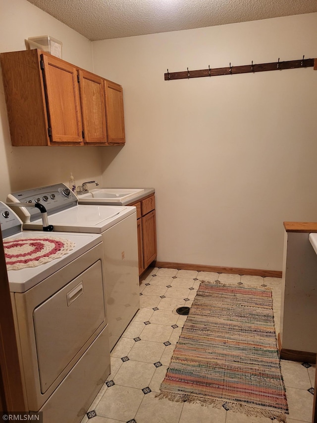 laundry area with cabinet space, washer and dryer, a textured ceiling, and baseboards