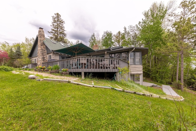 rear view of property with a chimney, a deck, and a lawn