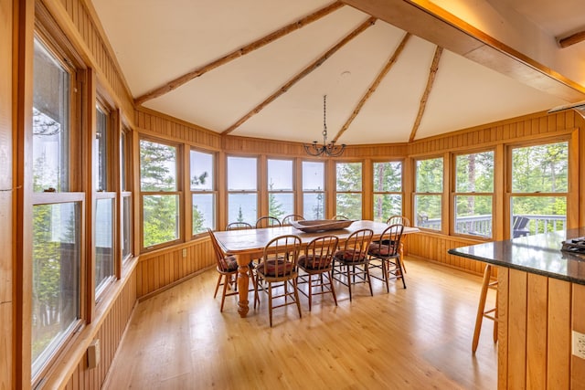 dining room featuring a water view, wooden walls, light wood-style flooring, and lofted ceiling with beams
