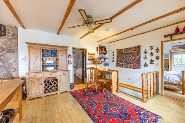 living area featuring light wood-type flooring, beamed ceiling, and ceiling fan