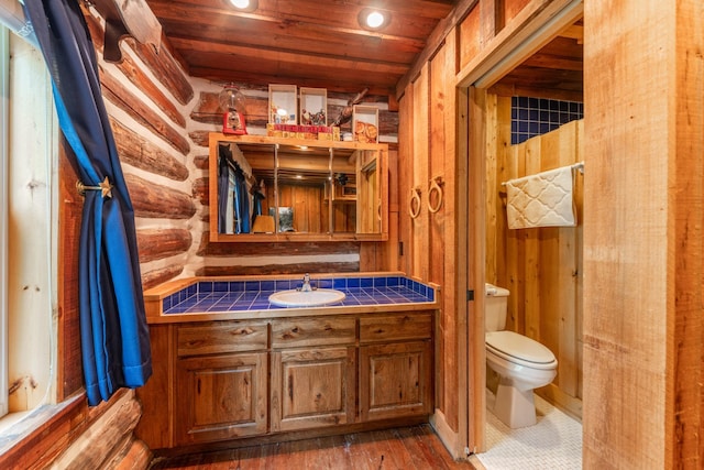 bathroom with vanity, toilet, wooden ceiling, wood finished floors, and log walls