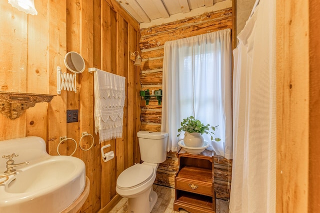 bathroom with toilet, log walls, and a sink