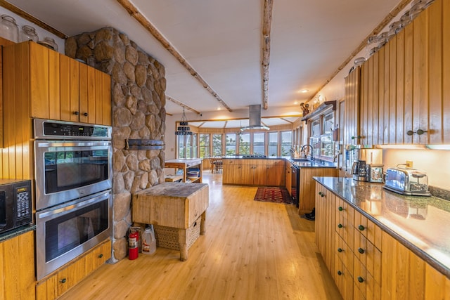 kitchen featuring light wood-style floors, black microwave, island exhaust hood, a sink, and stainless steel double oven