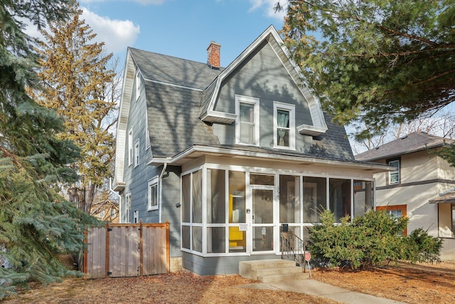 view of front of house with a sunroom, roof with shingles, a gambrel roof, and a chimney