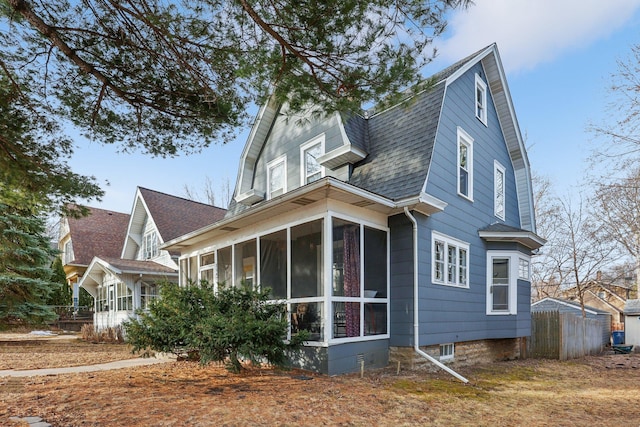 back of property with fence, a gambrel roof, a sunroom, and a shingled roof