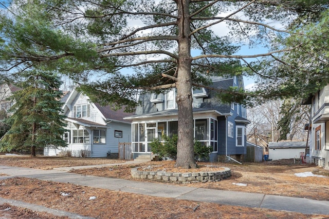 view of front of house with mansard roof, a sunroom, and a shingled roof
