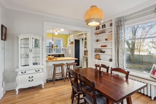 dining area with built in shelves, light wood-style floors, and ornamental molding
