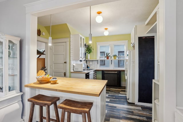 kitchen featuring butcher block countertops, white appliances, a peninsula, a kitchen bar, and dark wood finished floors