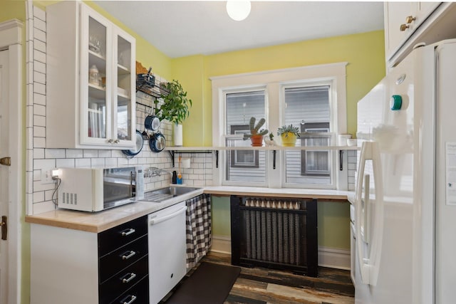 kitchen featuring white appliances, glass insert cabinets, dark wood-type flooring, a sink, and decorative backsplash