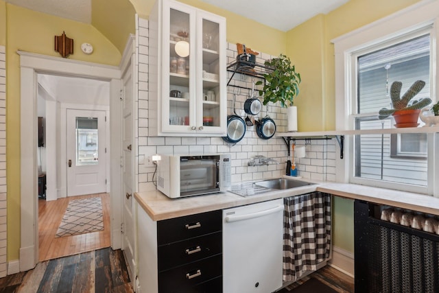 kitchen with white dishwasher, a sink, dark cabinetry, dark wood-style floors, and backsplash