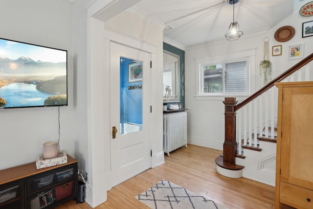 foyer entrance featuring light wood-type flooring, radiator heating unit, crown molding, and stairs