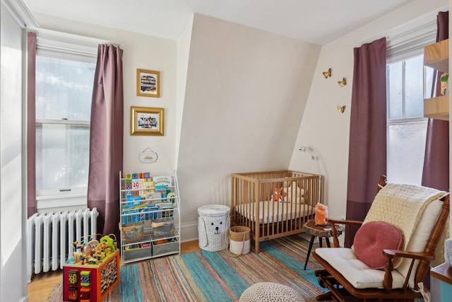 bedroom with radiator, wood finished floors, and a crib