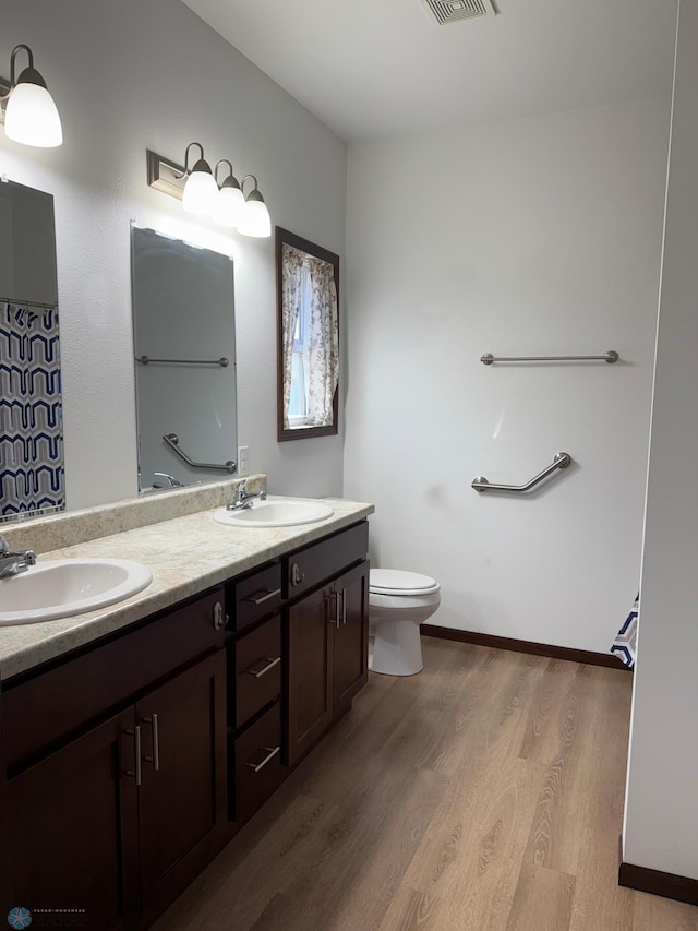 bathroom featuring a sink, toilet, double vanity, and wood finished floors