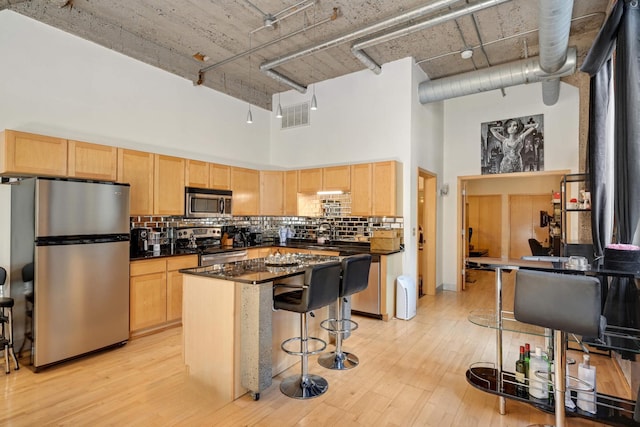 521 7th St Unit 311, Minneapolis, MN 55415 - kitchen featuring light brown cabinetry, dark countertops, backsplash, a high ceiling, and appliances with stainless steel finishes
