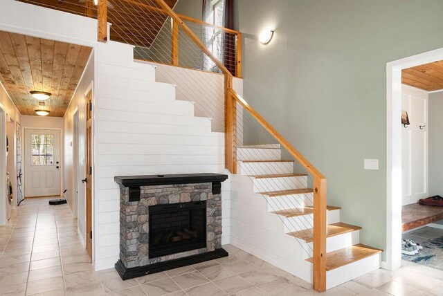 stairway featuring a stone fireplace and wood ceiling