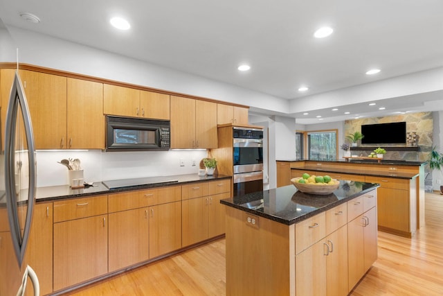 kitchen with double oven, light wood-type flooring, black microwave, and a center island