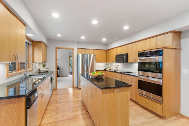 kitchen featuring a center island, a sink, black appliances, light wood finished floors, and dark stone counters