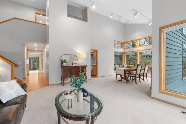 living room featuring track lighting, visible vents, a towering ceiling, baseboards, and carpet flooring
