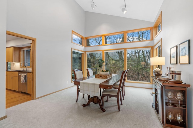dining area featuring high vaulted ceiling, baseboards, rail lighting, and light colored carpet