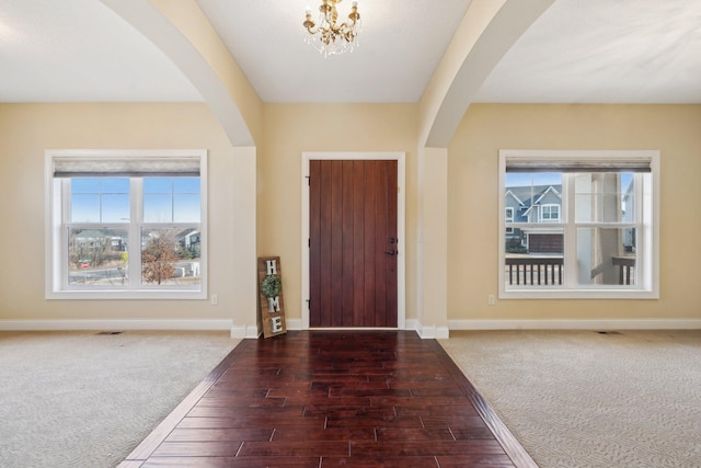 foyer featuring baseboards, arched walkways, a notable chandelier, and wood finished floors
