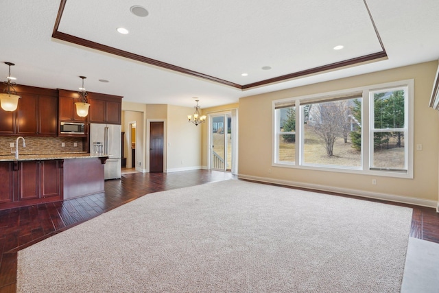 unfurnished living room featuring crown molding, a tray ceiling, a chandelier, and dark wood finished floors