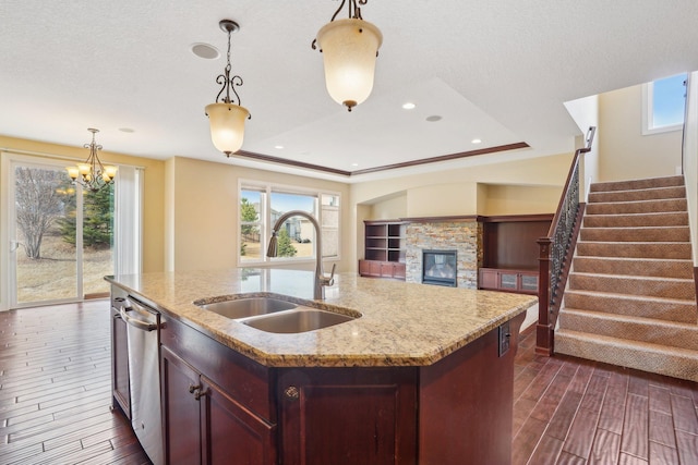 kitchen with dark wood-type flooring, a stone fireplace, a chandelier, a sink, and open floor plan