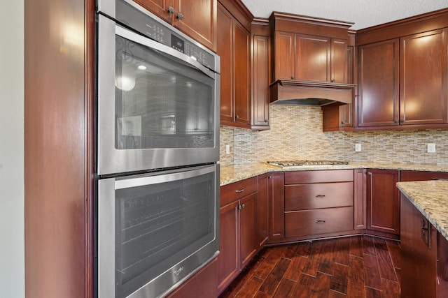 kitchen featuring light stone countertops, dark wood-type flooring, custom range hood, backsplash, and stainless steel appliances