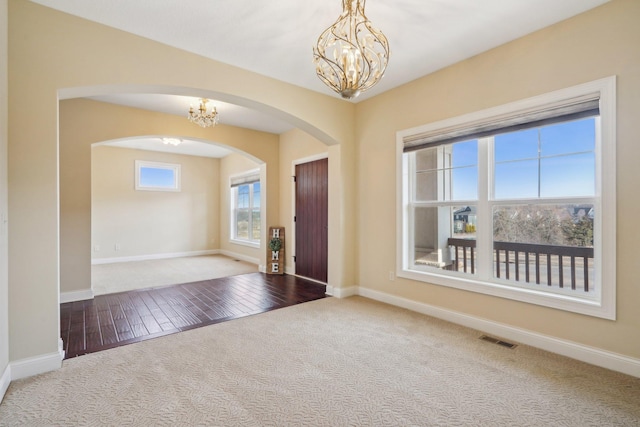 entryway with arched walkways, visible vents, carpet floors, a chandelier, and baseboards