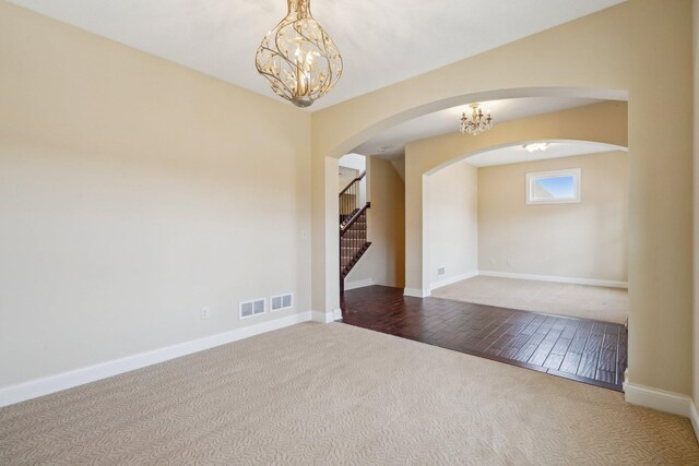 spare room featuring visible vents, arched walkways, a notable chandelier, stairs, and carpet flooring