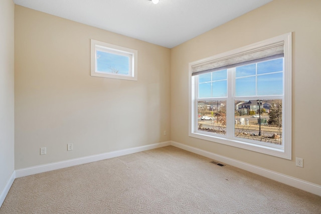 carpeted spare room featuring plenty of natural light, visible vents, and baseboards