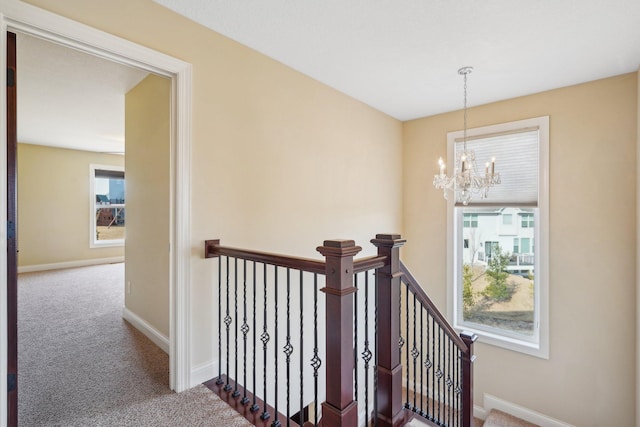 corridor featuring carpet flooring, a notable chandelier, and an upstairs landing