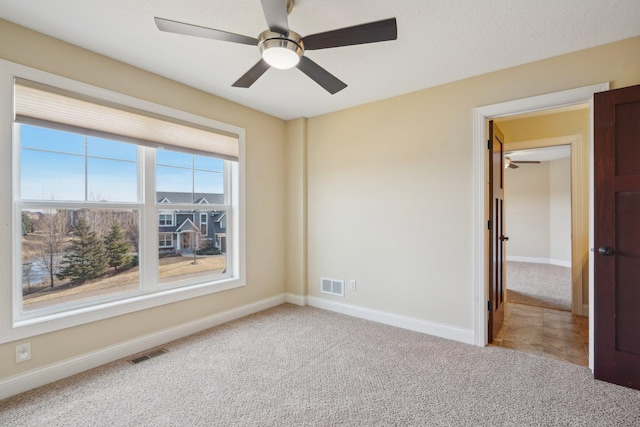 empty room with baseboards, carpet flooring, ceiling fan, and visible vents