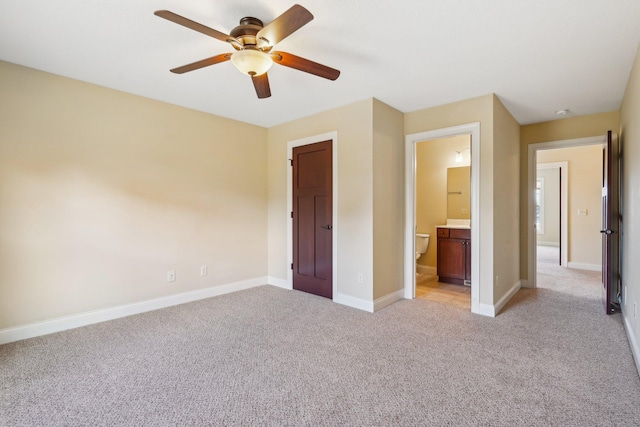 unfurnished bedroom featuring ensuite bathroom, light colored carpet, baseboards, and a ceiling fan