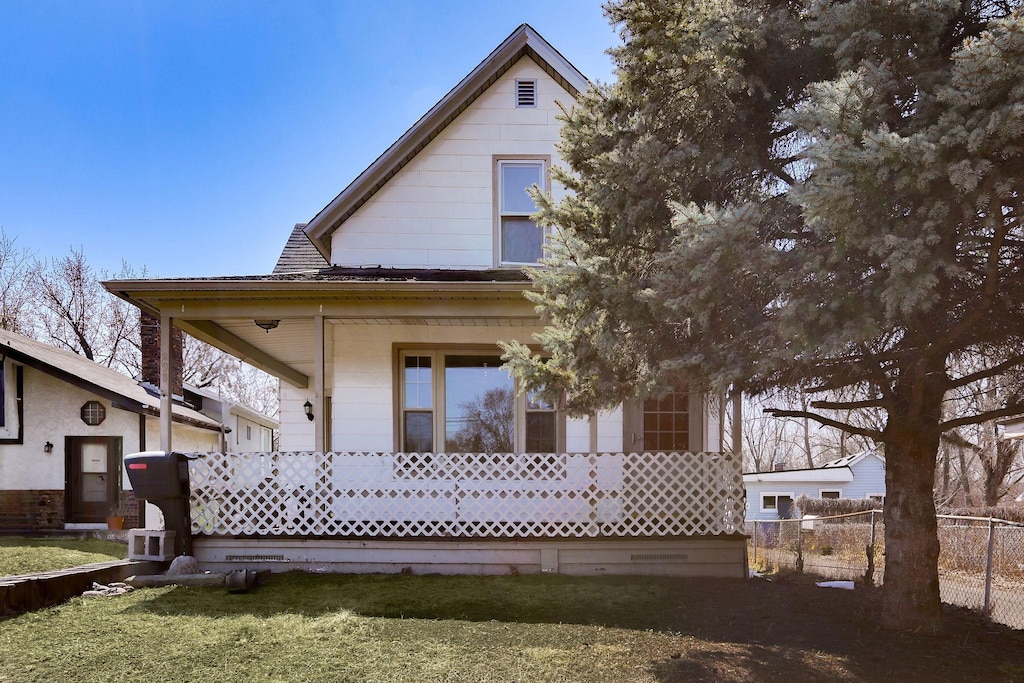 back of property with covered porch, fence, and a lawn